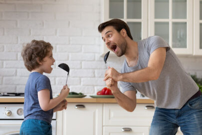 Parent and child sing in the kitchen using spoons as microphones.