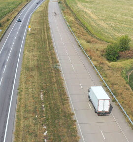 Semi truck driving down a long highway surrounded by fields.