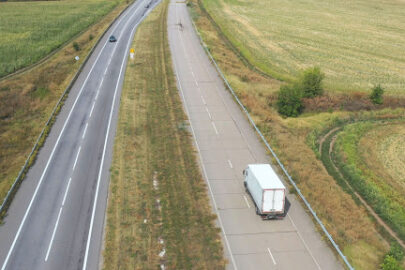 Semi truck driving down a long highway surrounded by fields.