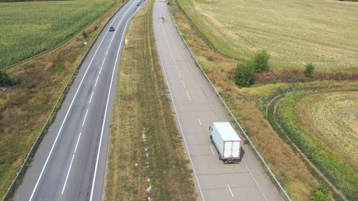 Semi truck driving down a long highway surrounded by fields.