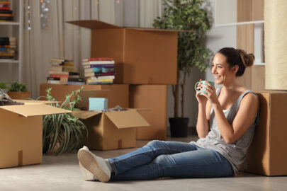 Happy tenant resting drinking coffee moving home sitting on the floor in the night.