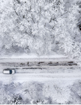 One vehicle driving through the winter snowy forest on a country road.