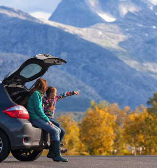 A mother and daughter sitting in their car, looking at mountains.