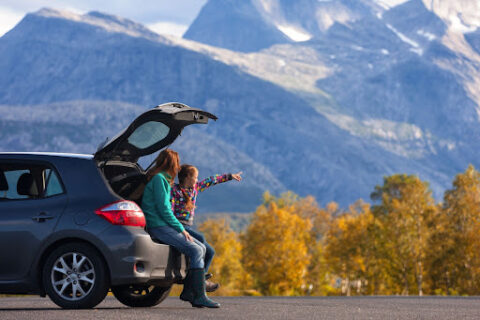 A mother and daughter sitting in their car, looking at mountains.