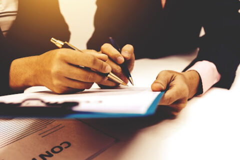 Two hands holding pens and a clipboard.