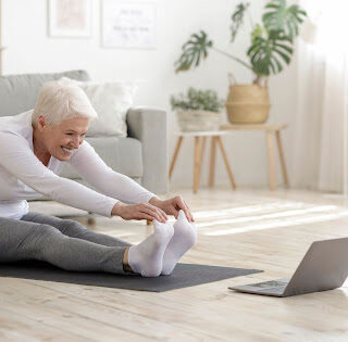 An elderly woman stretching on a yoga mat.