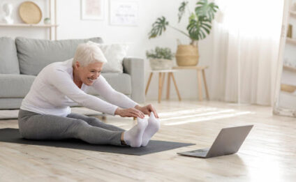 An elderly woman stretching on a yoga mat.