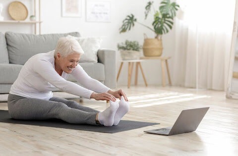 An elderly woman stretching on a yoga mat.