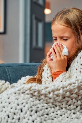 A little girl blows her nose while wrapped in a blanket.