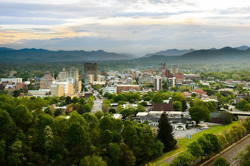 The skyline of downtown Asheville, North Carolina at sunset with mountains in the background.
