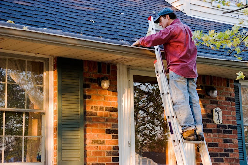 Man on a ladder cleaning gutters.