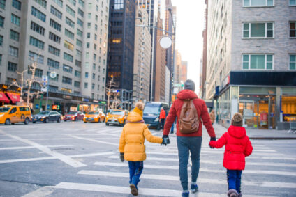 A dad holds hands with his two kids as they cross the street in NYC.