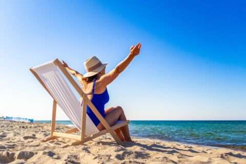 A woman sits on a beach chair in front of the ocean with her arms wide.
