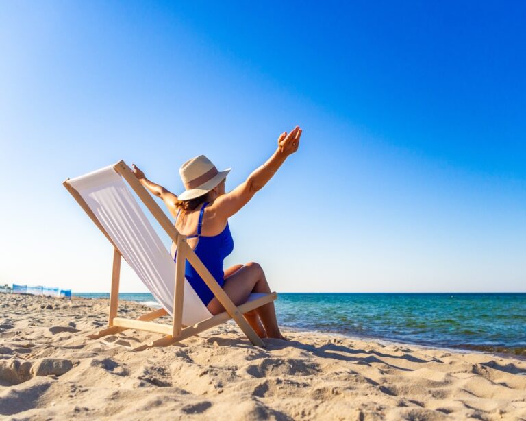 A woman sits on a beach chair in front of the ocean with her arms wide.